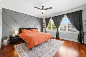 Master bedroom with gray geometric patterned accent wall and a bed with a coral colored bedspread.