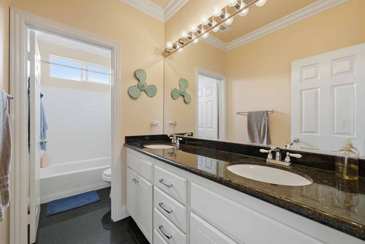 Full bathroom with double-vanity and a tub/shower combo in the background.