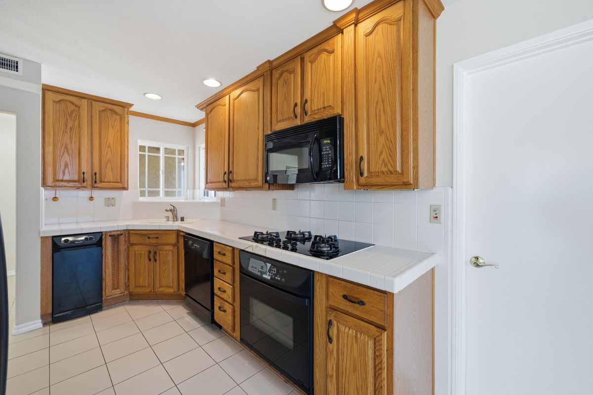Kitchen with oak cabinetry, white counters and black appliances.