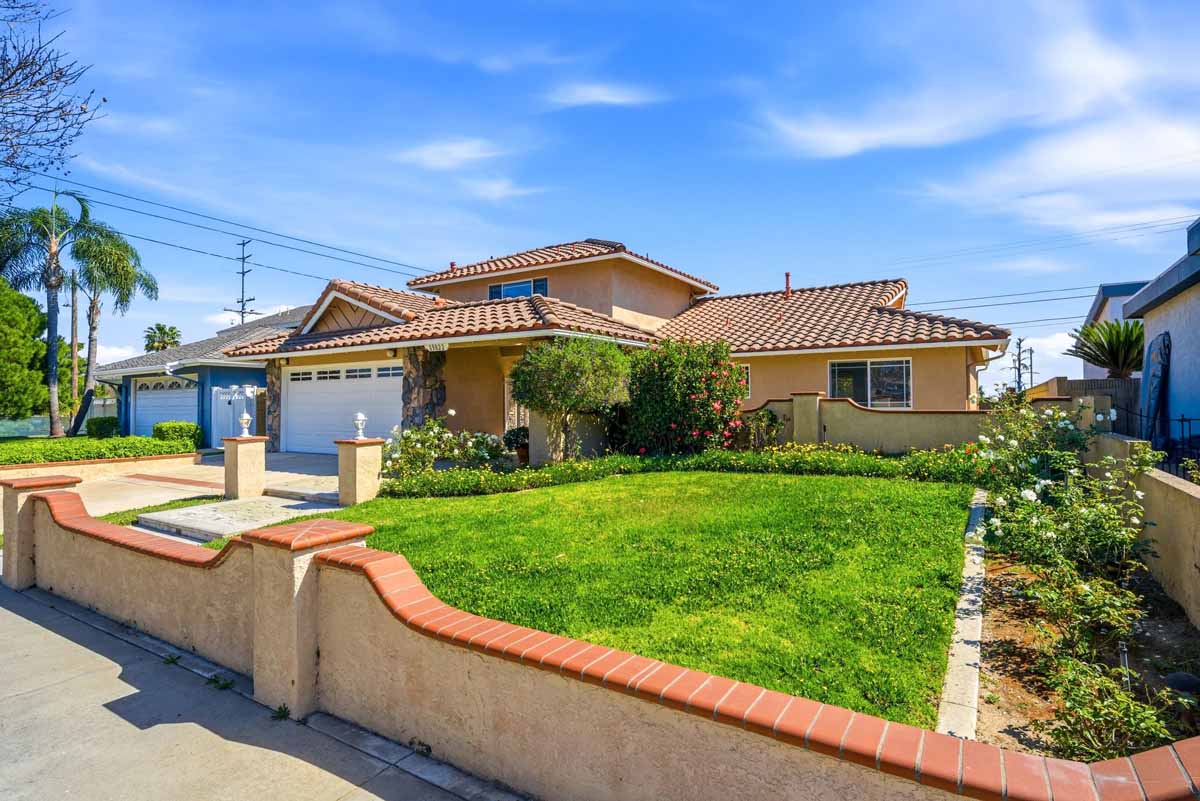 Exterior view of 19022 Summerfield Lane, Huntington Beach with tan painted stucco, a grass lawn, and a white garage door.