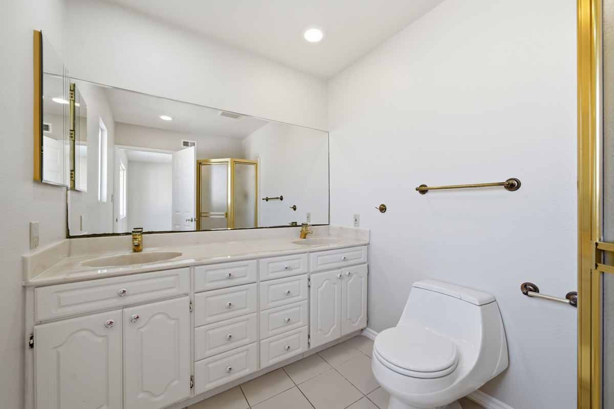 White bathroom with a double sink vanity and a toilet.