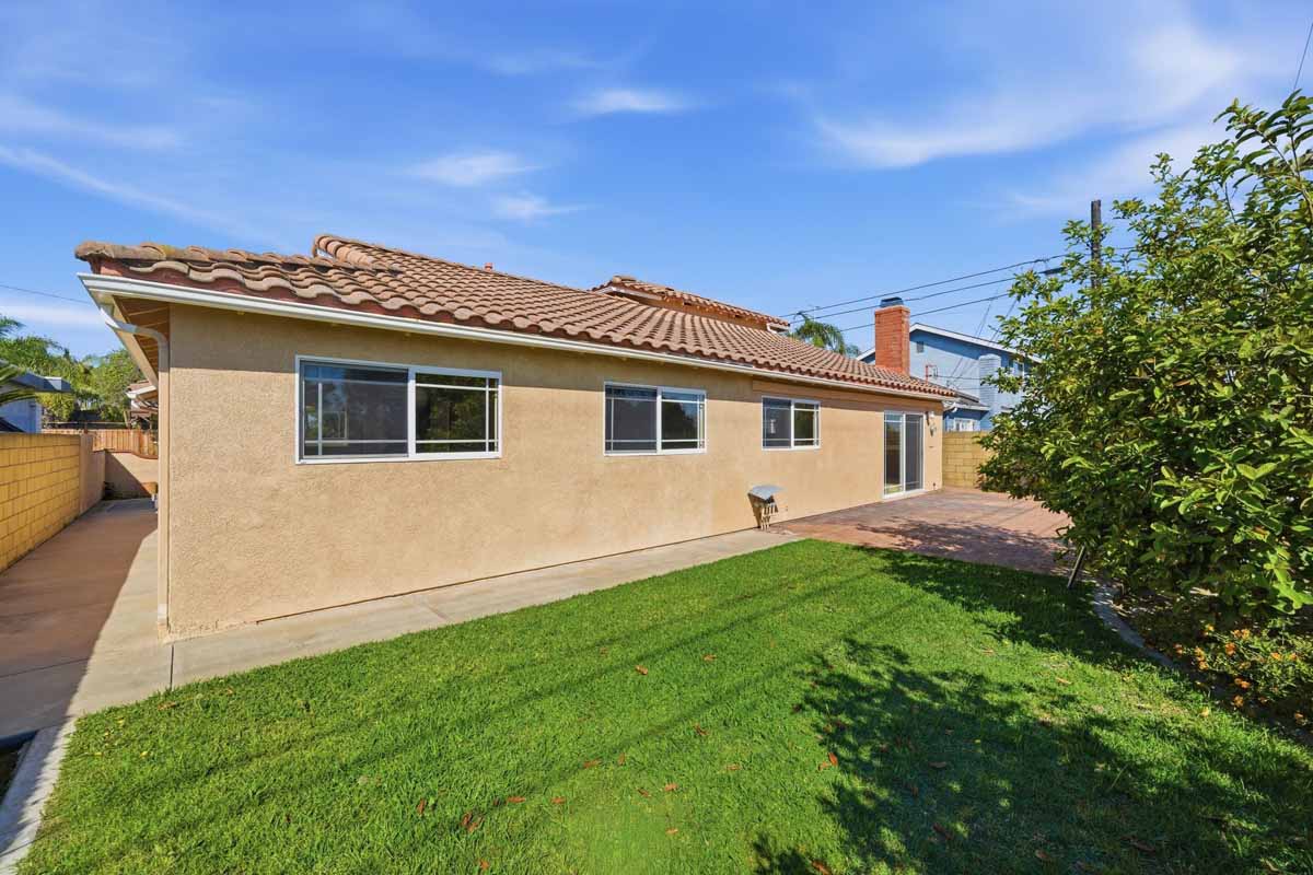 Green grass in a backyard with a tan stuccoed back wall of a home showing.