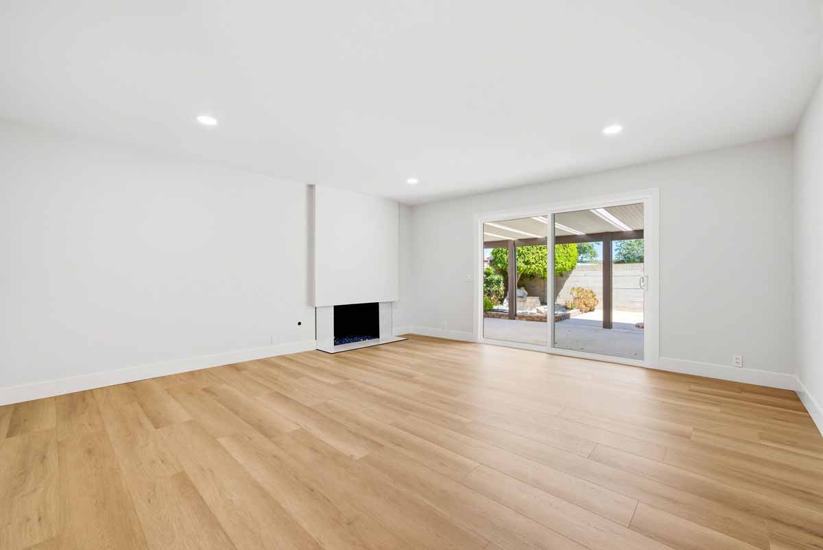 Updated living space with new light-toned wood flooring and a fireplace next to a sliding glass door to the backyard.