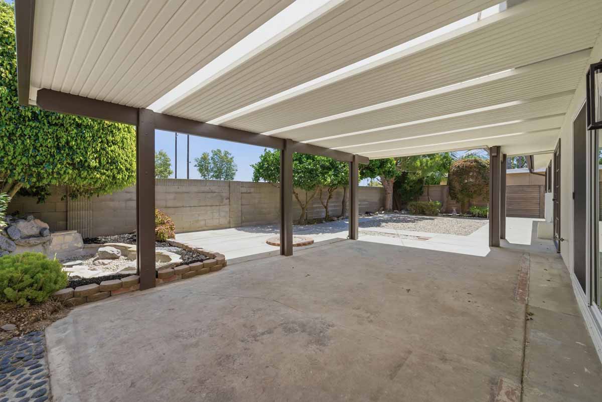 A large covered patio with concrete and trees surrounding the backyard.