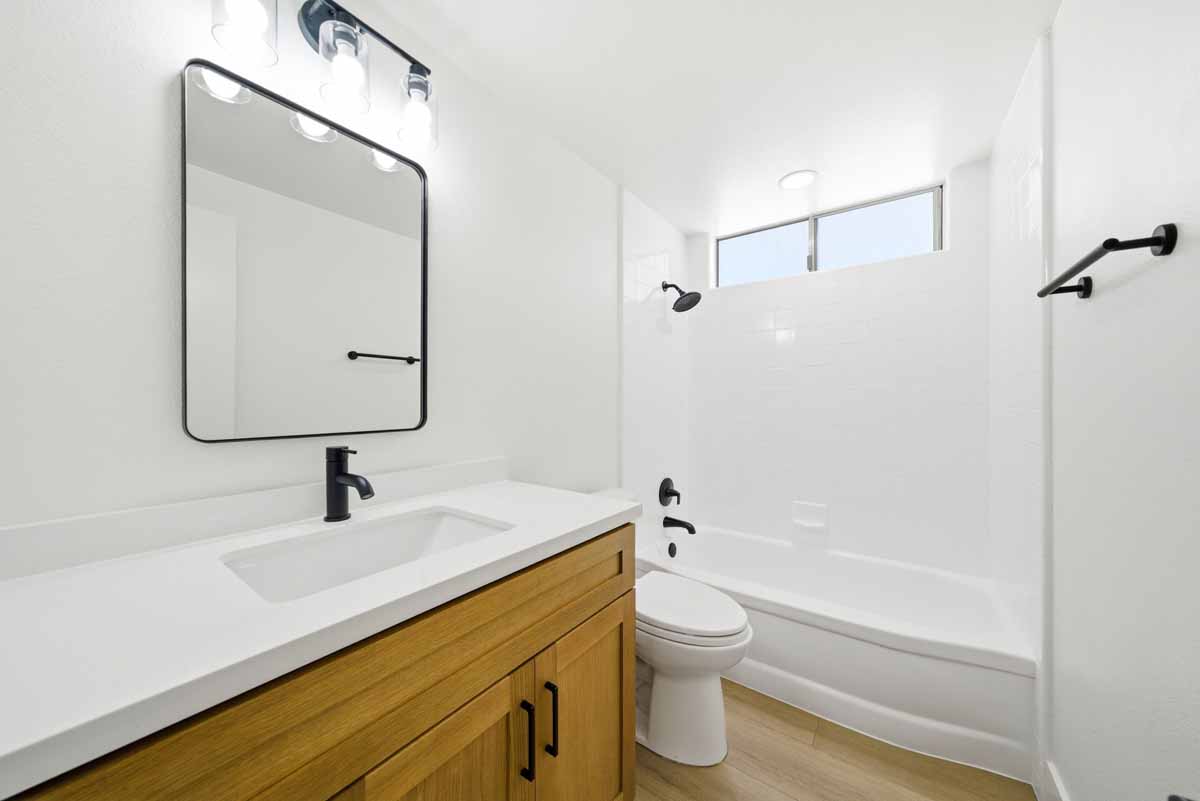 A remodeled full bathroom with a wood cabinet with white countertops and black fixtures.