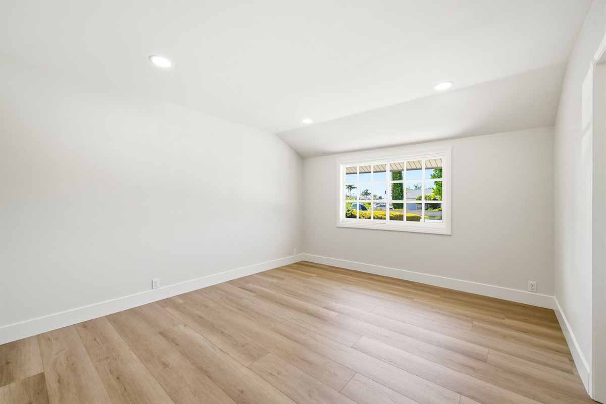 An empty bedroom with new light-wood flooring, recessed lighting and a window.