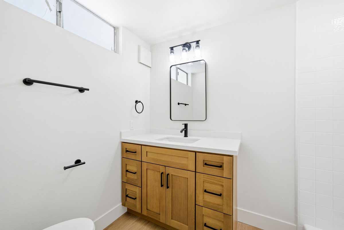 A remodeled full bathroom with a wood cabinet with white countertops and black fixtures.