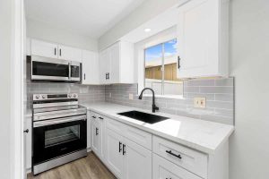 Updated kitchen with new stainless appliances, white cabinets and stone counter top, with a black sink and fixtures.