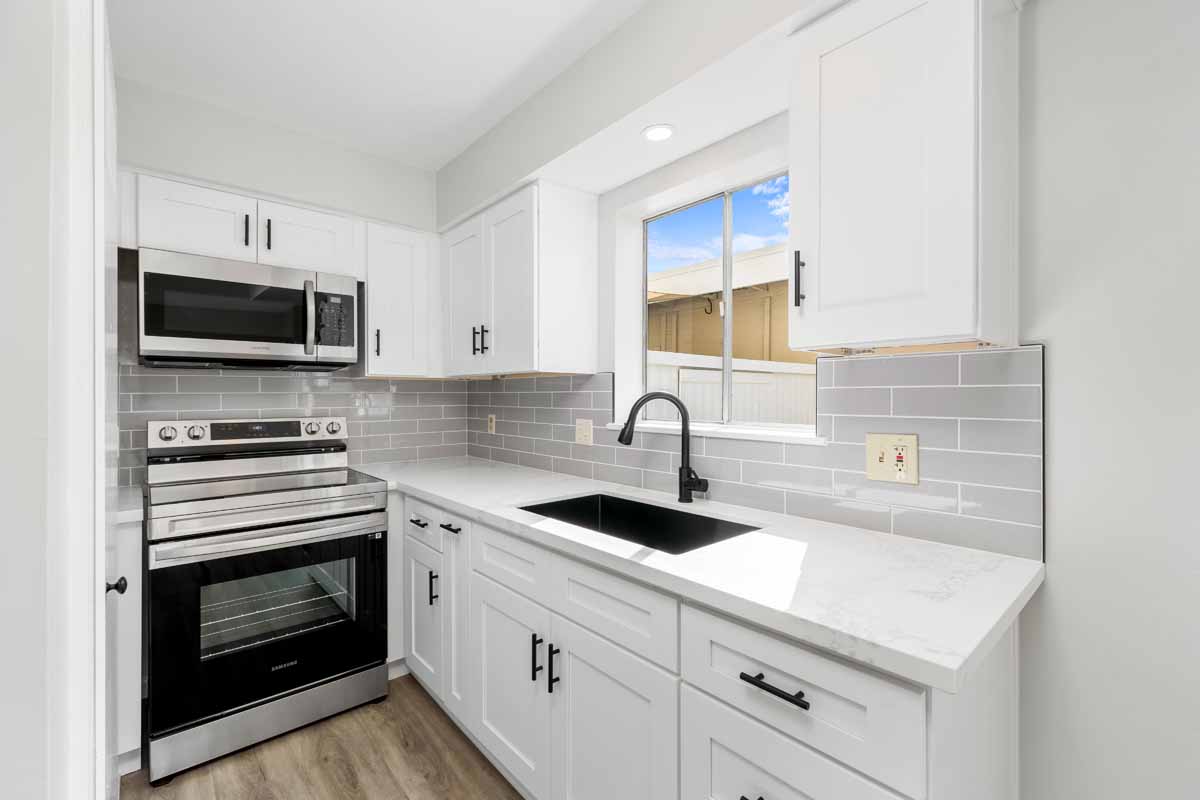 Updated kitchen with new stainless appliances, white cabinets and stone counter top, with a black sink and fixtures.