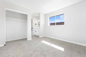 Bright, white, newly renovated bedroom with new light colored flooring, white walls and a small window.