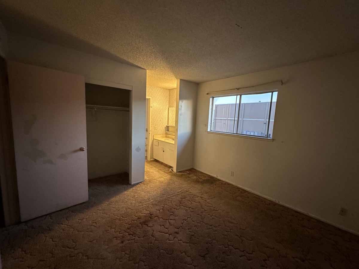 Dark outdated room with brown carpet, neutral colored walls and a small window.