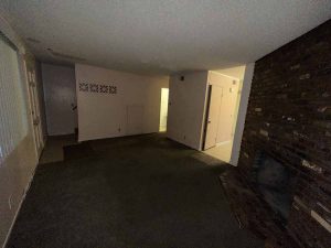 Dark, outdated living room with dark colored carpet and neutral wall color.