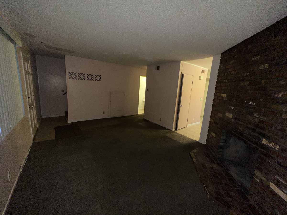 Dark, outdated living room with dark colored carpet and neutral wall color.
