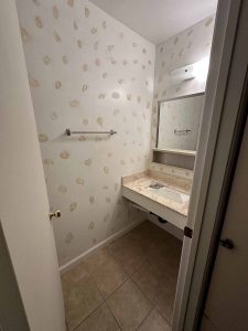An outdated bathroom with floral wallpaper and a beige vanity.
