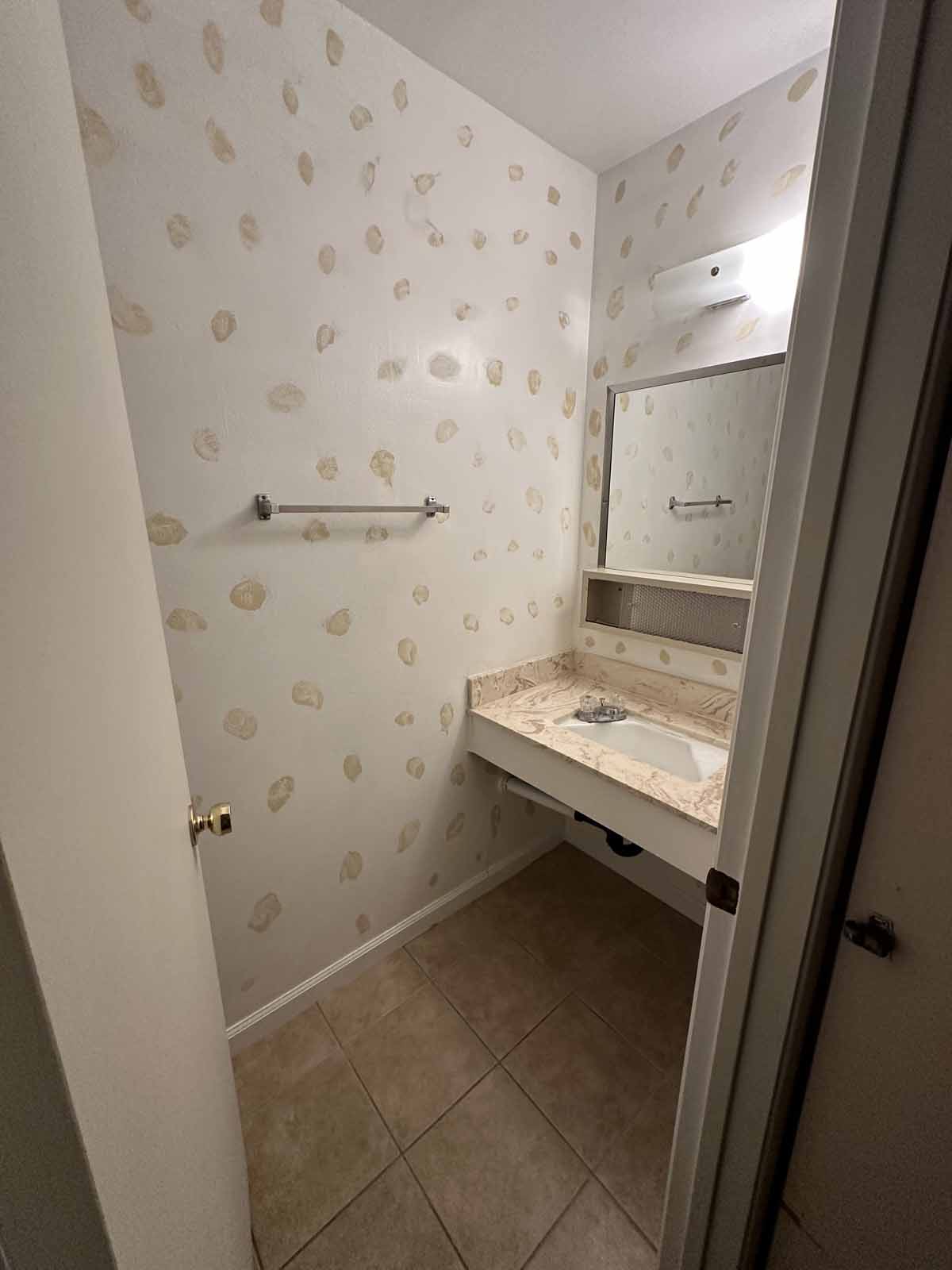 An outdated bathroom with floral wallpaper and a beige vanity.