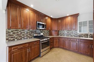 A kitchen with dark wood cabinetry, multi-colored mosaic tile backsplash, and stainless steel appliances.