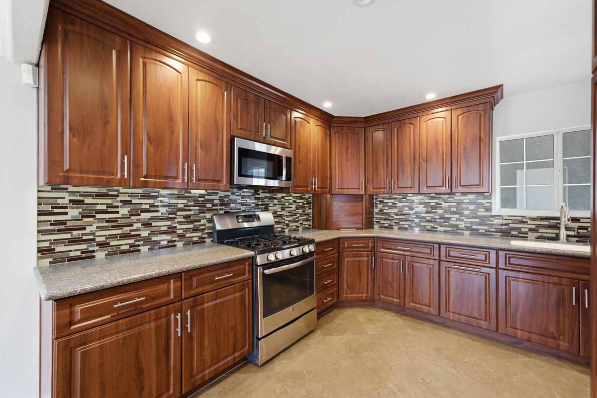 A kitchen with dark wood cabinetry, multi-colored mosaic tile backsplash, and stainless steel appliances.