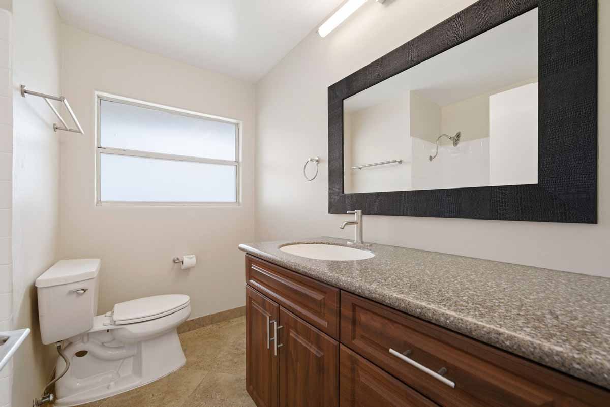 A bathroom with a white toilet, a brown cabinet vanity with a light brown stone counter top.
