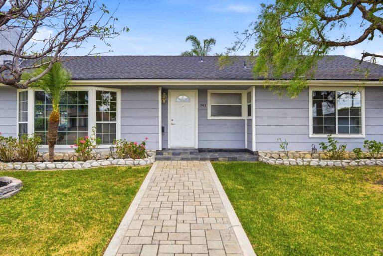 Exterior front view of home with gray paint, a white door, and grass on wither side of the walkway.