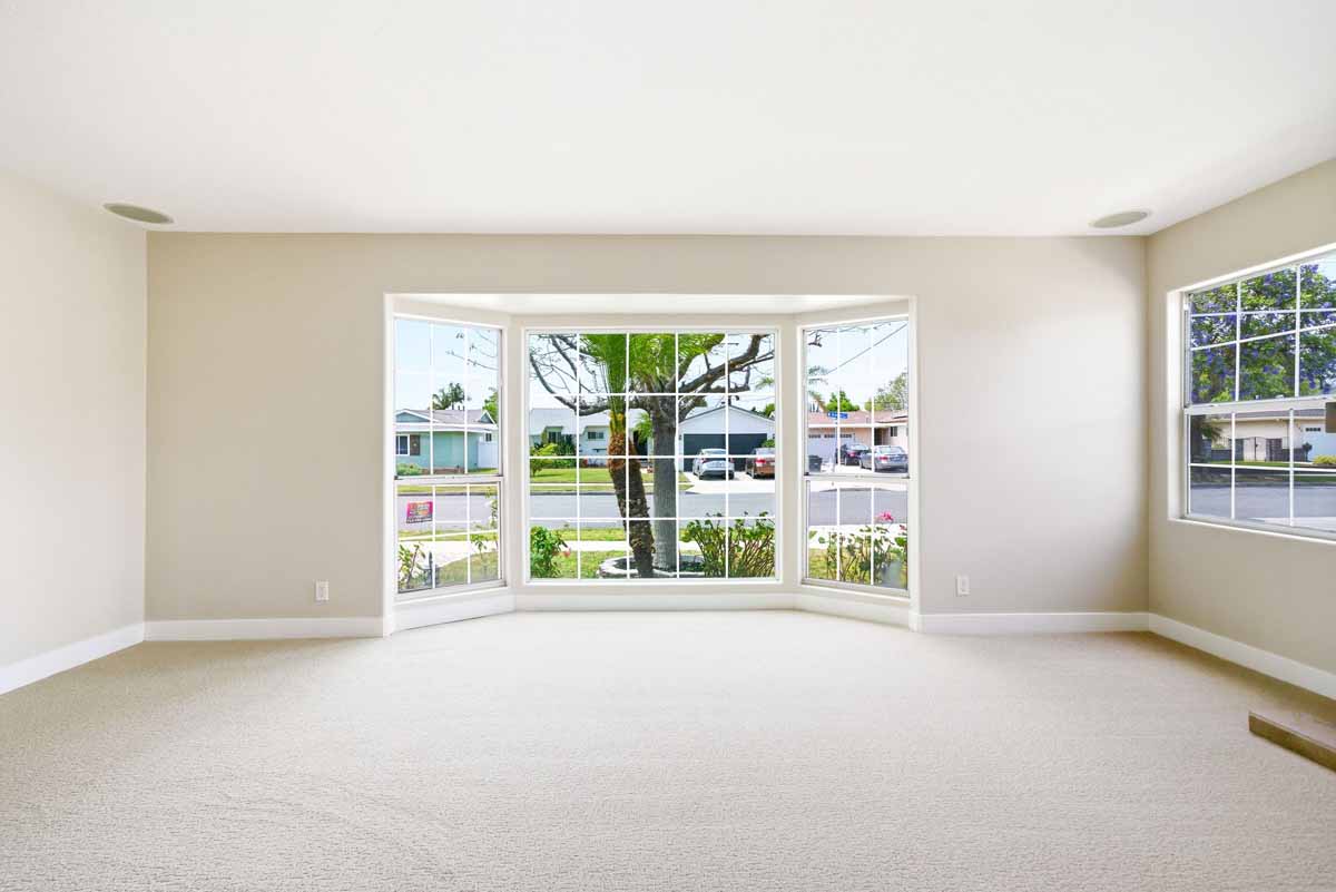 Empty living room with clean, light colored carpet and a large bay window overlooking the front yard.
