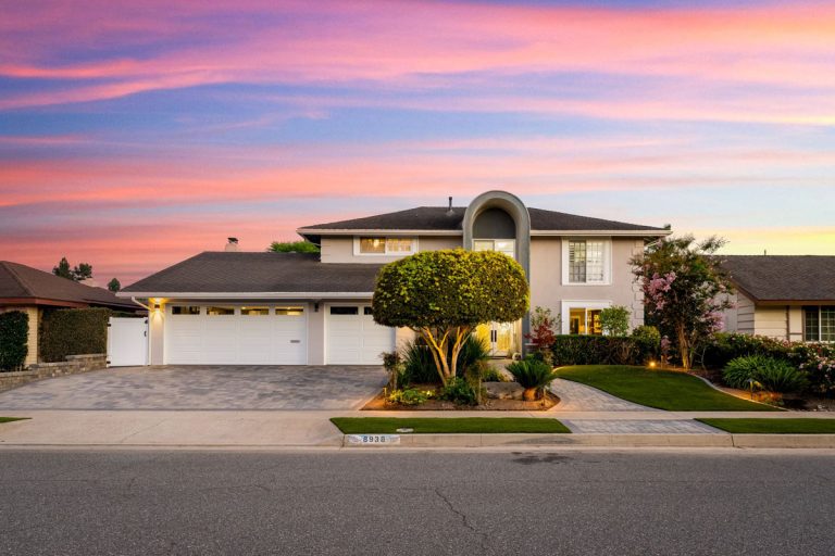A large two story home with 3-car white garage doors, and a beige exterior with a pink and purple sky in the background.
