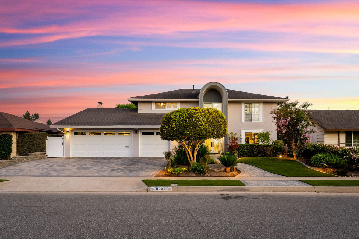 A large two story home with 3-car white garage doors, and a beige exterior with a pink and purple sky in the background.