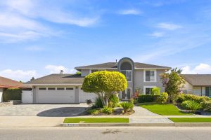 View of 8938 Martin Avenue, Fountain Valley from the street showing neutral paint, white garage doors, and a large tree.