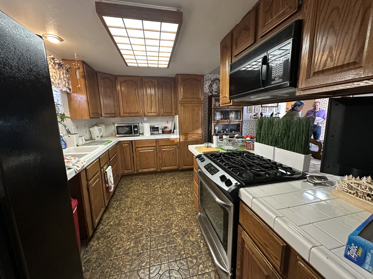 Outdated kitchen with linoleum flooring, darker wood cabinetry and overhead fluorescent lighting.