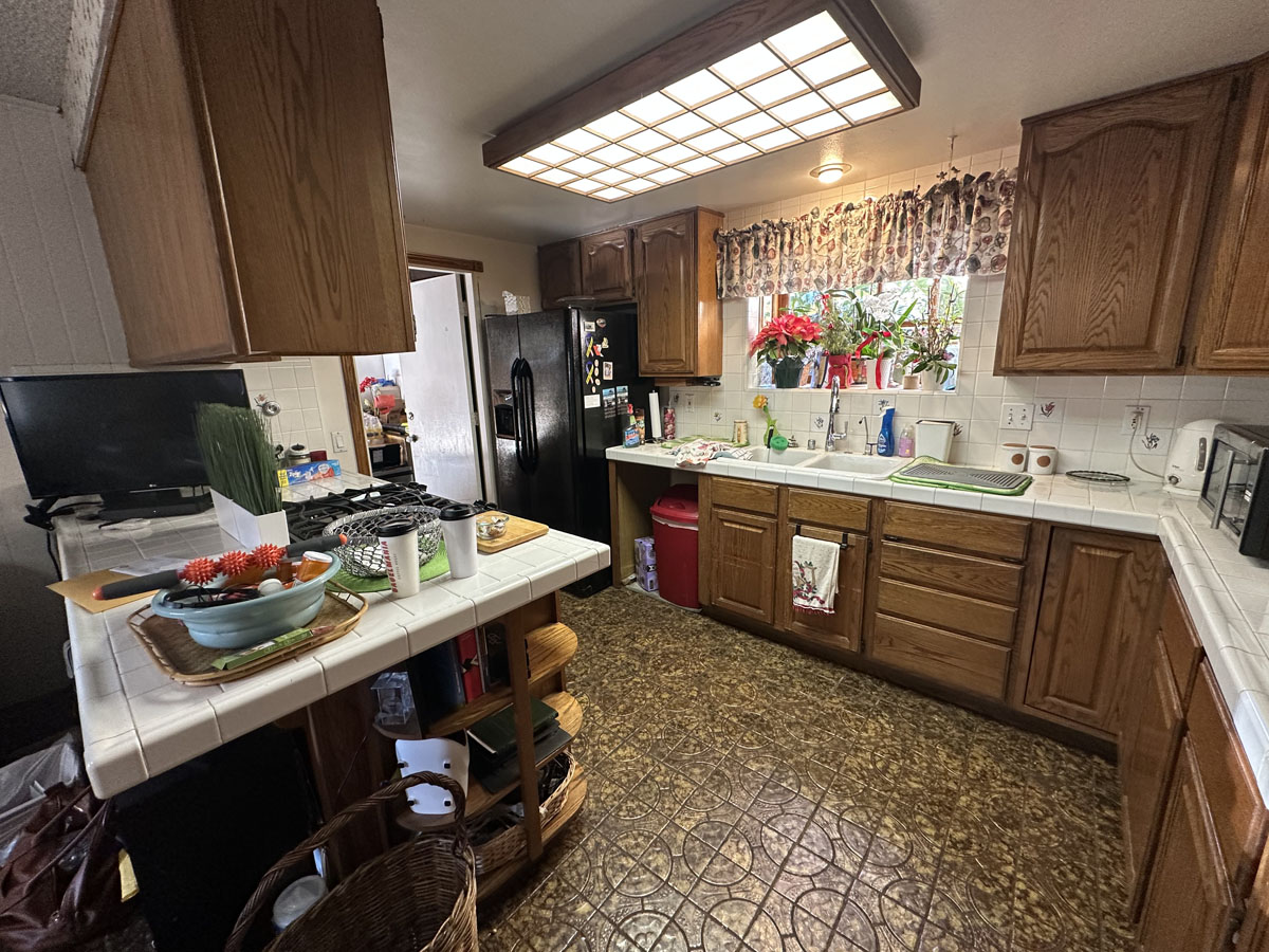 Outdated kitchen with linoleum flooring, darker wood cabinetry and overhead fluorescent lighting.