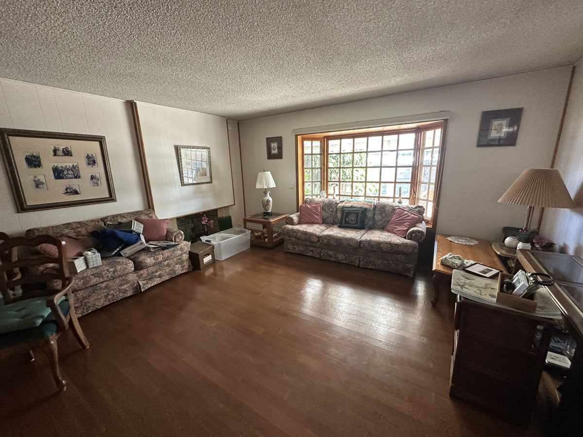 Outdated living room with wood floors and a big window on the back wall.