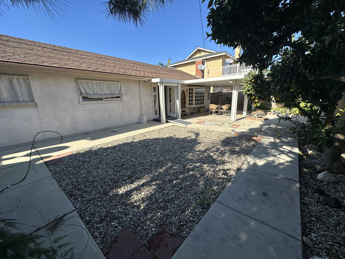 Original backyard space with dead grass and stained paint on the exterior of house.