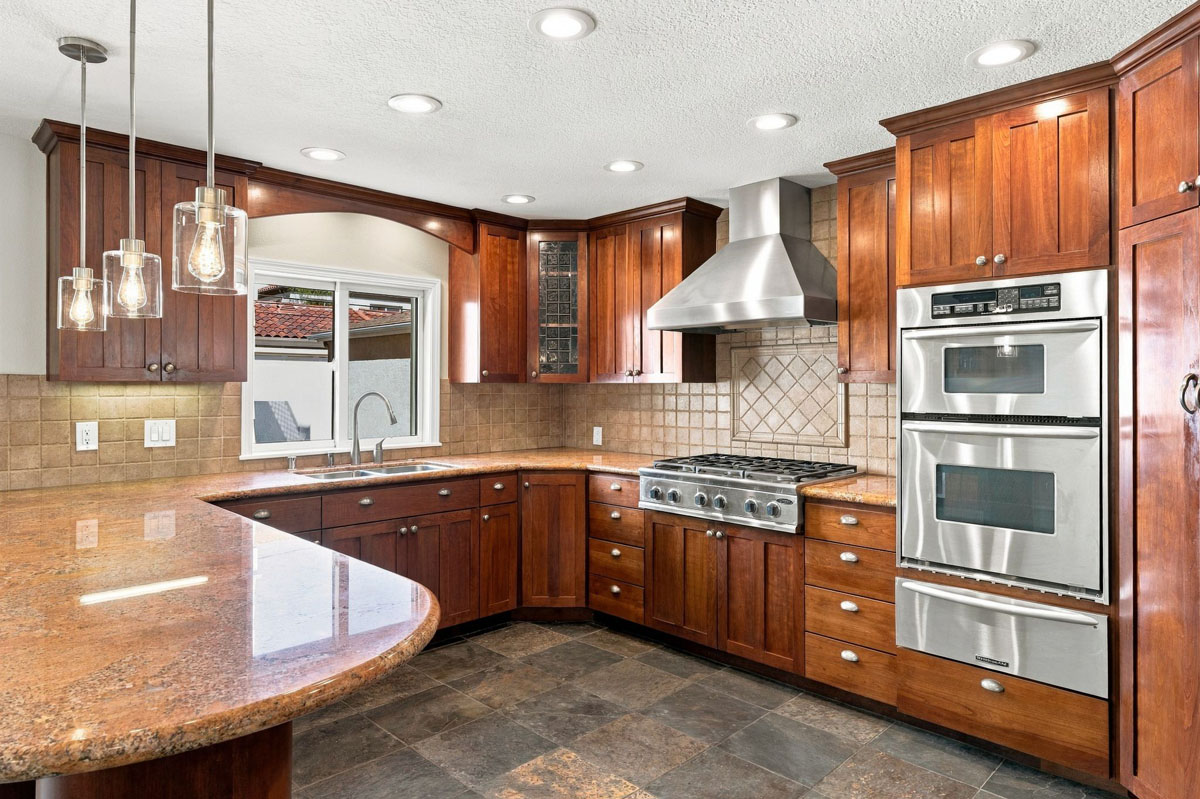 Kitchen with darker wood cabinetry, tan stone counters, and stainless steel appliances.