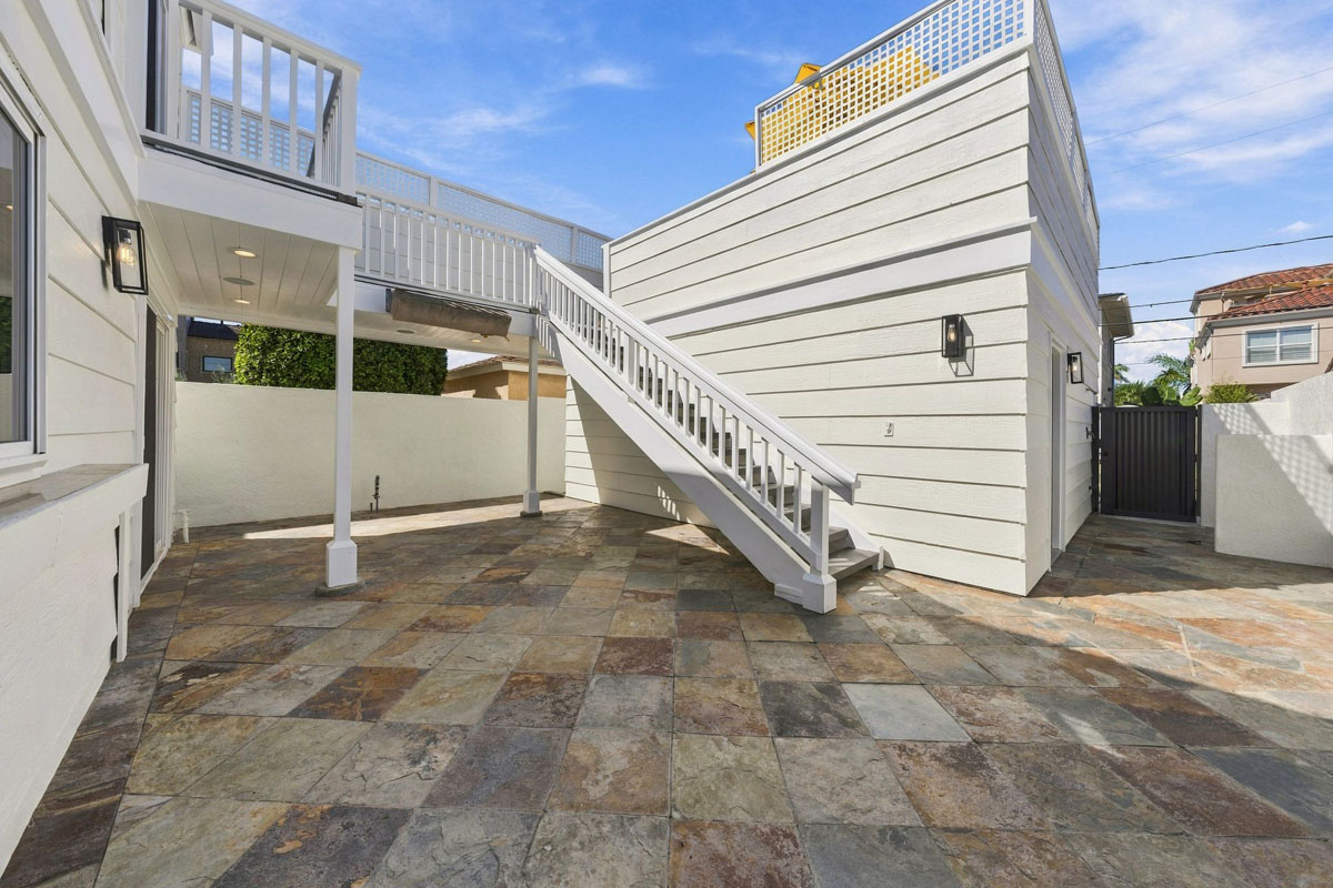 Back yard with tiled hardscape and a staircase leading to the roof top balcony and second level decks.