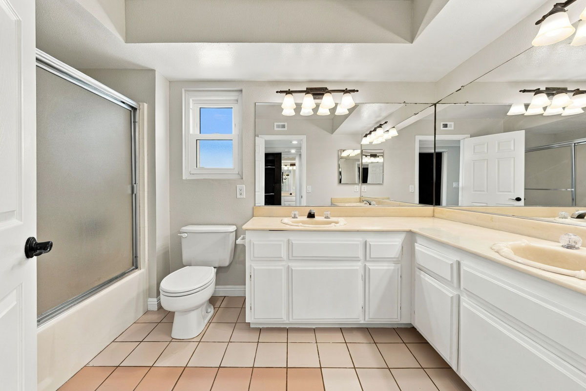 Master bathroom with tiled flooring, toilet, L-shaped vanity with two sinks, and a walk-in shower.